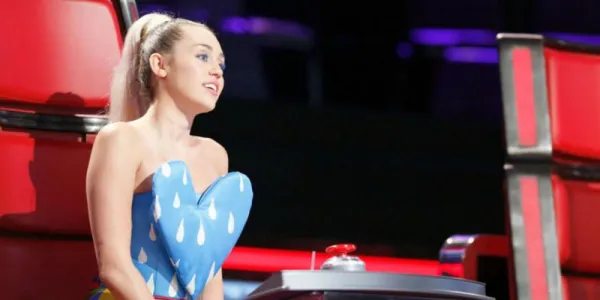   The Voiceの椅子に座っているマイリー・サイラスは、大きなハートの形をしたシャツを着て、横を向いています.