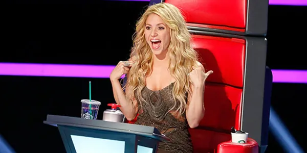   The Voice の椅子に座っているシャキーラは、肩に手を置き、口を大きく開けています。